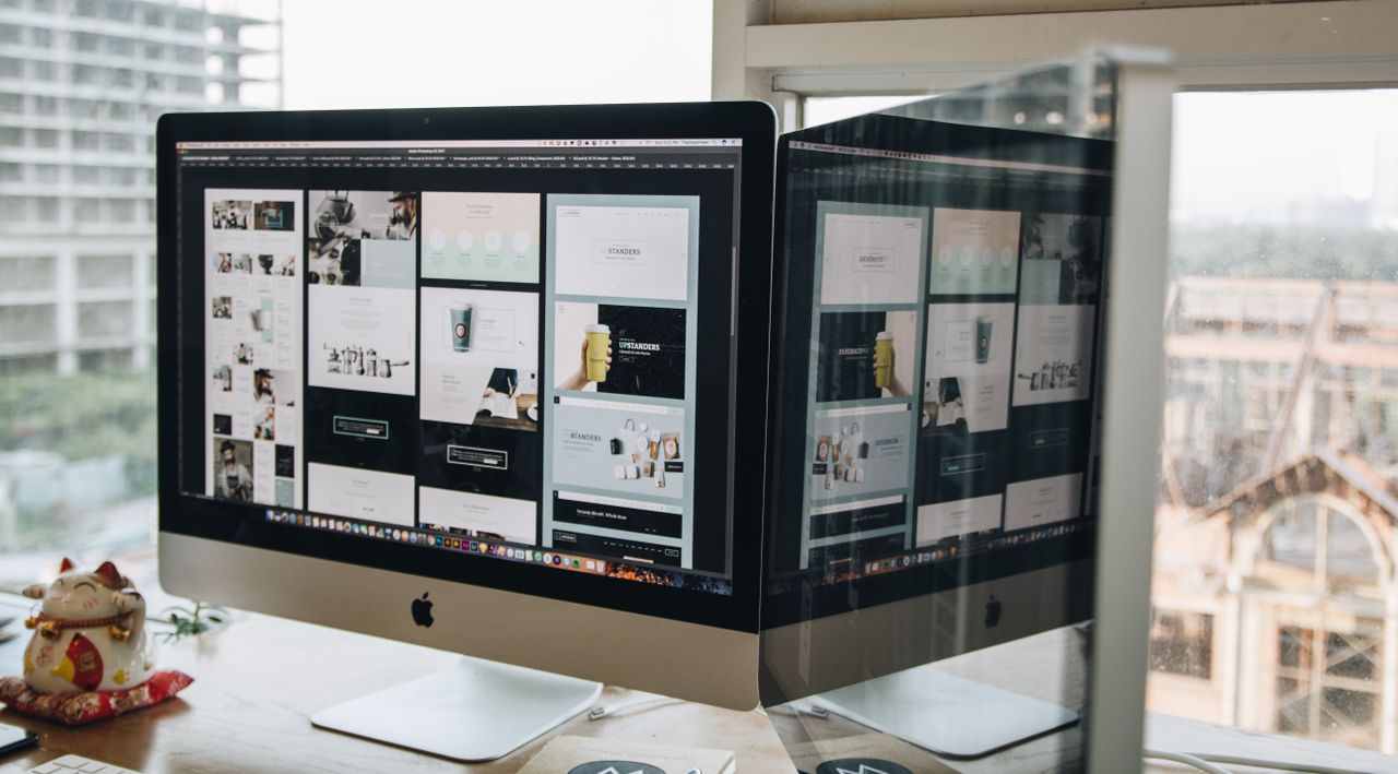 contact-img Dual monitors on a desk, showcasing web design in a modern office setting.